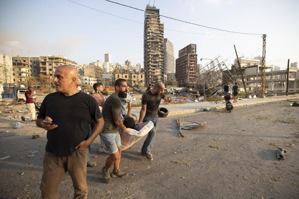 People carry a wounded after a massive explosion in Beirut, Lebanon, Tuesday, Aug. 4, 2020. Massive explosions rocked downtown Beirut on Tuesday, flattening much of the port, damaging buildings and blowing out windows and doors as a giant mushroom cloud rose above the capital. Witnesses saw many people injured by flying glass and debris. (AP Photo/Hassan Ammar)