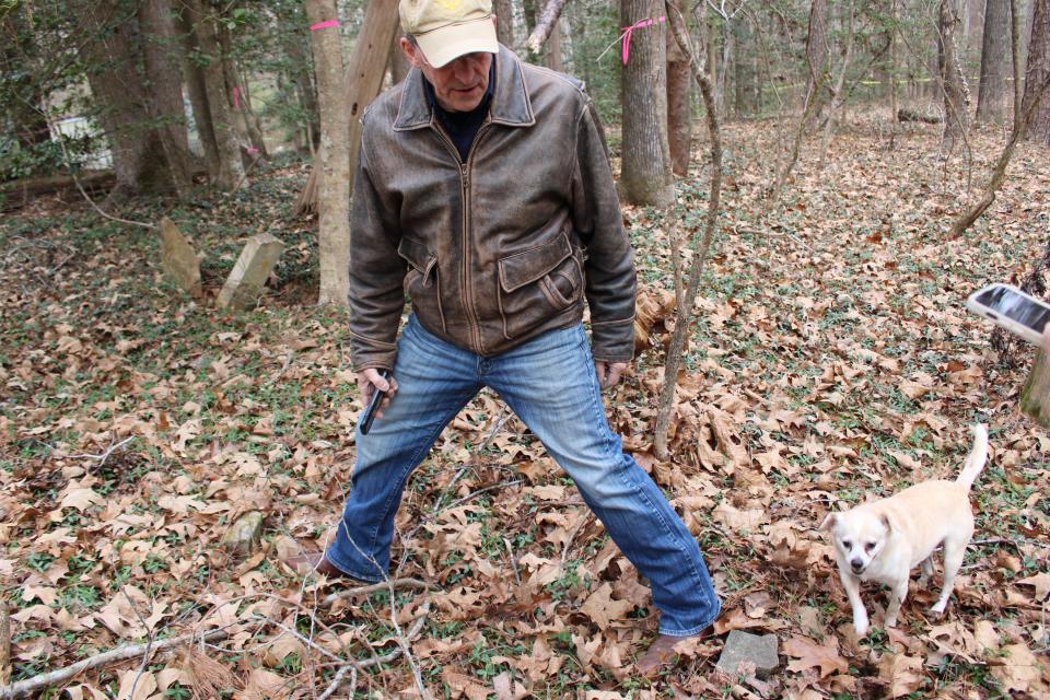 Archaeologist Michael Clem with Department of Historic Resources locates a grave in the Blick Cemetery which has two stone markers in Lawrenceville, Virginia. Thirteen-year-old Ginger standing nearby is Richard Blick's pet.