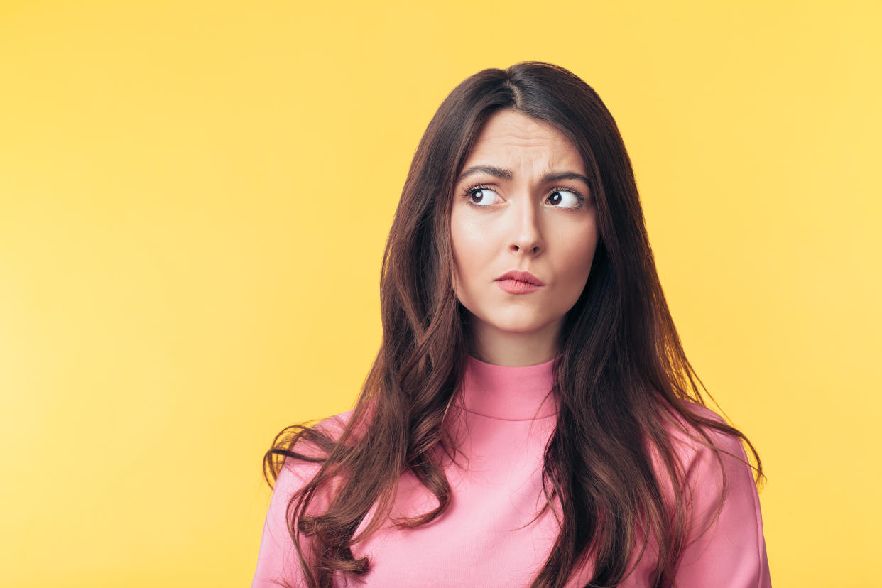 Thoughtful confused woman looking away isolated over yellow background. Doubt concept