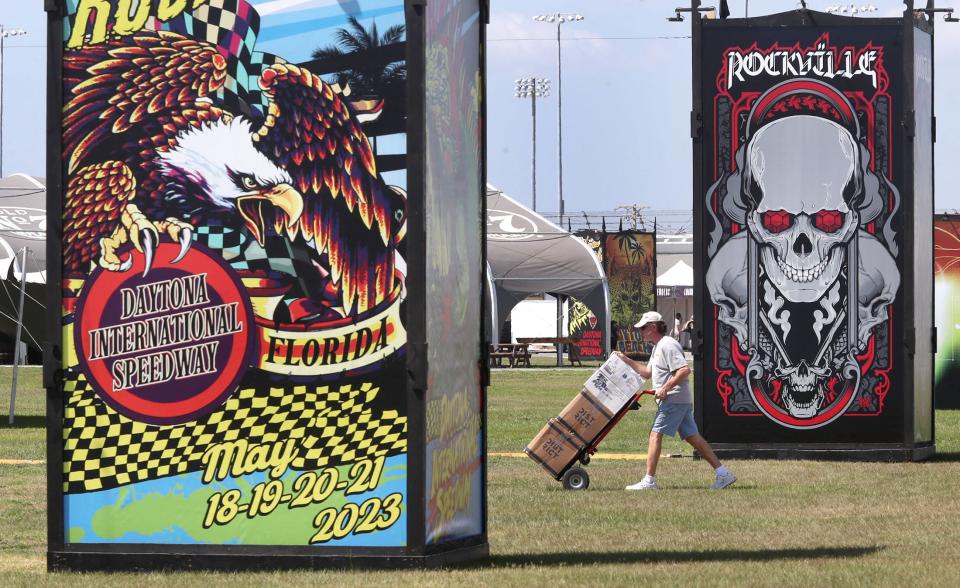 A vendor moves boxes past colorful signage as preparation is completed for the 2023 edition of Welcome to Rockville at Daytona International Speedway. The four-day heavy-metal fest returns May 9-12, generating sold-out rooms for Daytona Beach-area hotels.