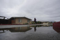 Ileana Miranda is reflected in a puddle while walking past a San Jerardo cooperative home in Salinas, Calif., Wednesday, Dec. 20, 2023. Some California farming communities have been plagued for years by problems with their drinking water due to nitrates and other contaminants in the groundwater that feeds their wells. (AP Photo/Jeff Chiu)