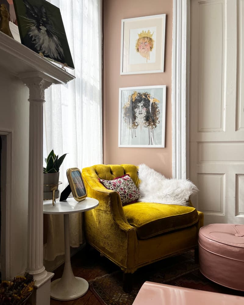 Gold velvet chair next to accept tulip table in corner of pink living room under artwork.