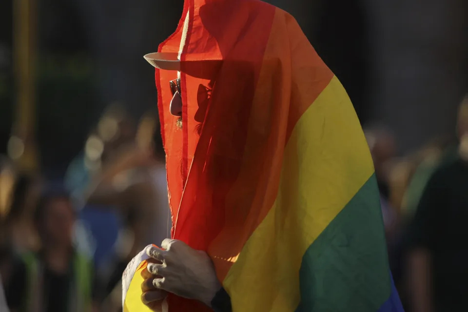 Bir protestocu, 8 Ağustos 2024 Perşembe günü Bulgaristan'ın Sofya kentinde, okullarda LGBTQ+ ve sözde geleneksel olmayan cinsel tercihler hakkında konuşmayı yasaklayan, bir gün önce kabul edilen tartışmalı bir yasal değişikliği kınamak için Bulgaristan parlamentosu dışında düzenlenen bir miting sırasında gökkuşağı bayrağı altında görülüyor. (AP Fotoğrafı/Valentina Petrova)