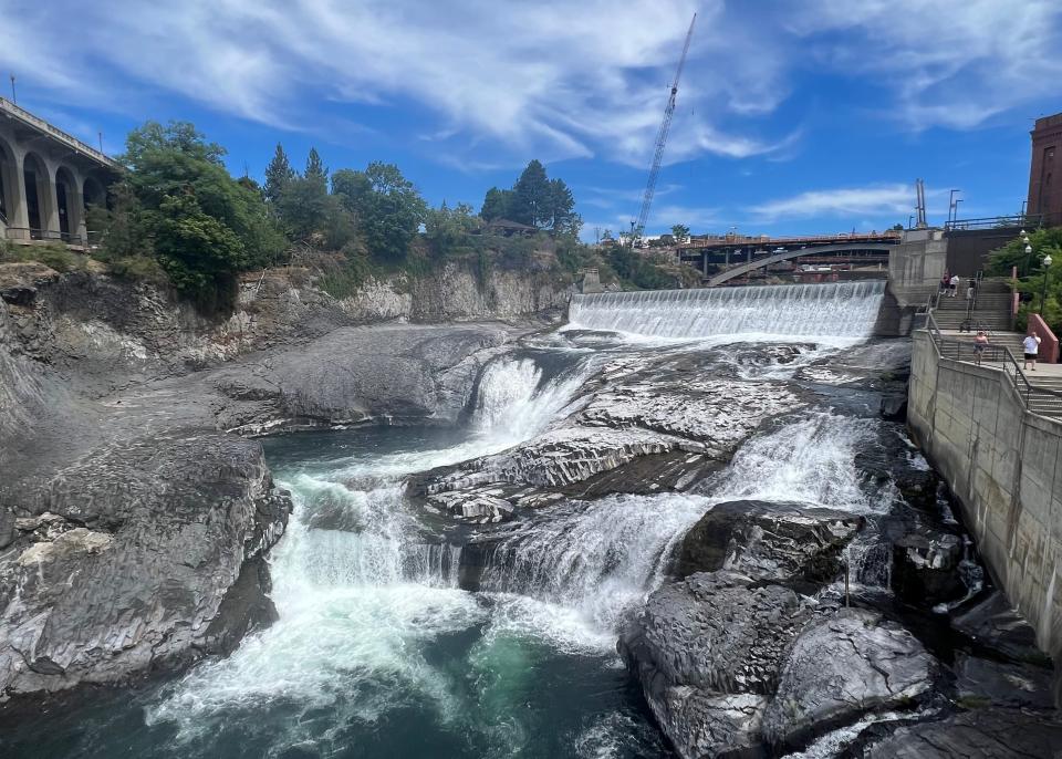 A waterfall with large rocks, trees, and an overpass.  