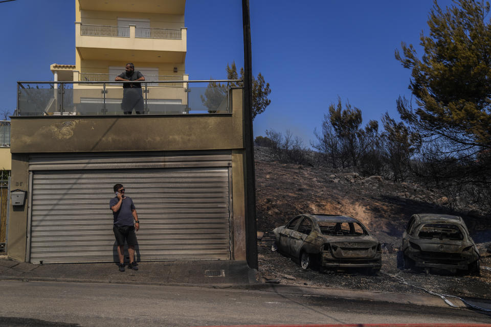 CORRECTS AREA'S NAME - A man speaks on his mobile phone as he stands next of two burned cars in the area of Panorama Palinis, eastern Athens, Wednesday, July 20, 2022. Hundreds of people were evacuated from their homes late Tuesday as a wildfire threatened mountainside suburbs northeast of Athens. Firefighters battled through the night, struggling to contain the blaze which was being intensified by strong gusts of wind. (AP Photo/Thanassis Stavrakis)