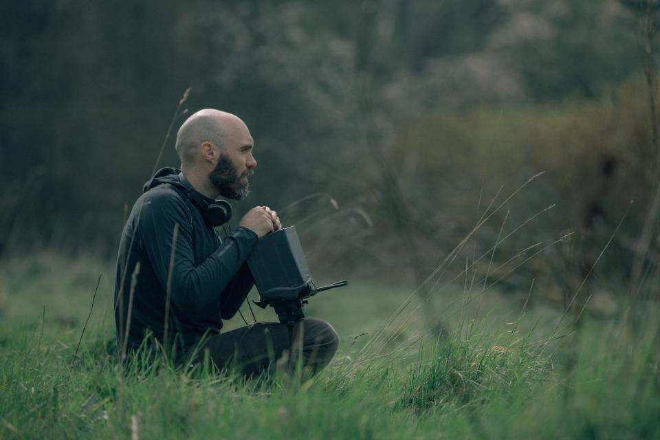 The Green Knight director David Lowery sits in a field with a camera