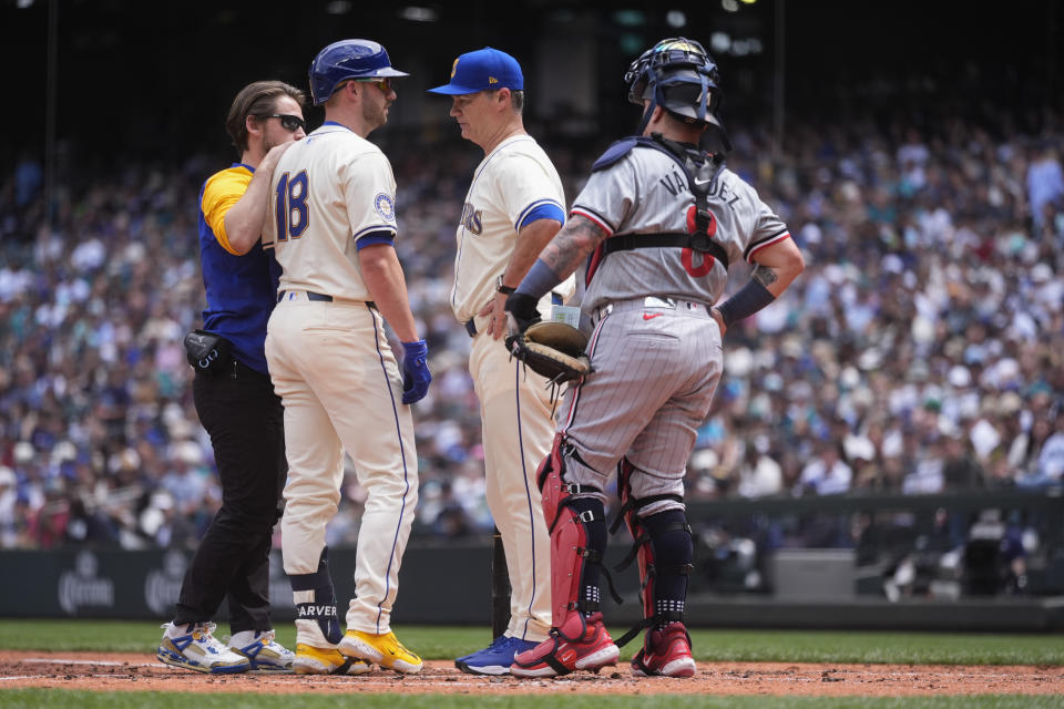 Seattle Mariners catcher Mitch Garver is checked on by a trainer and manager Scott Servais after being hit by a pitch as Minnesota Twins catcher Christian Vázquez looks on during the second inning of a baseball game Sunday, June 30, 2024, in Seattle. Garver would leave the game after the inning and was replaced in the batting order by Luis Castillo. (AP Photo/Lindsey Wasson)