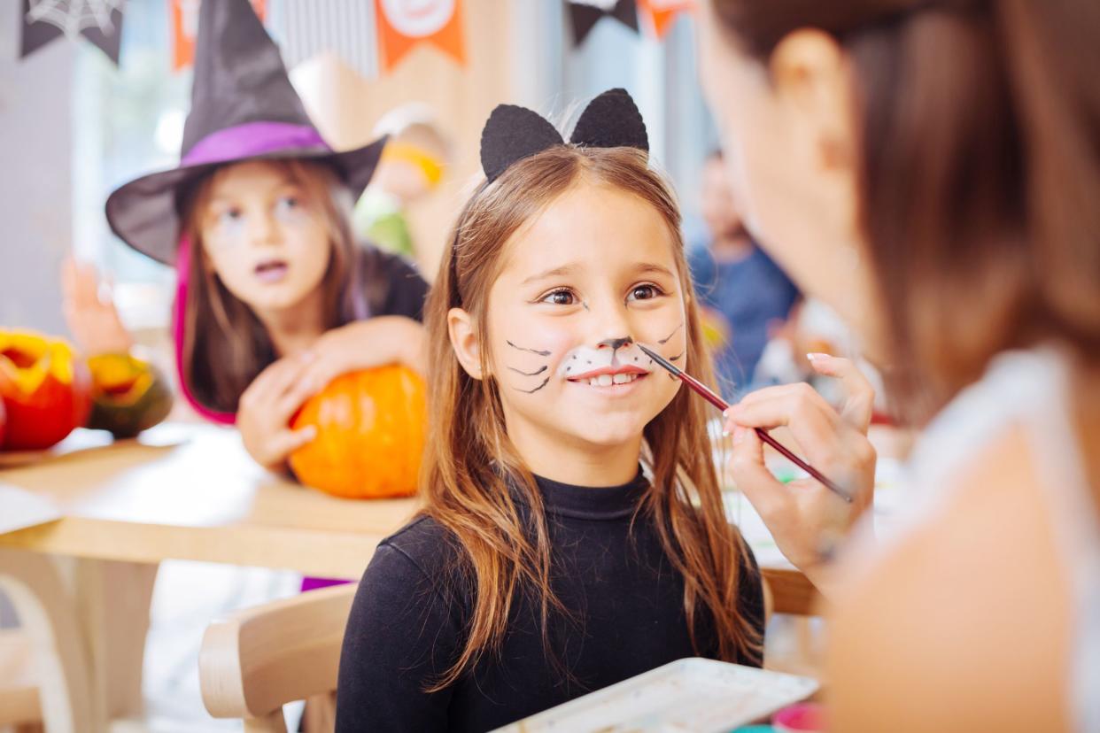 woman applying face paint to child in cat costume