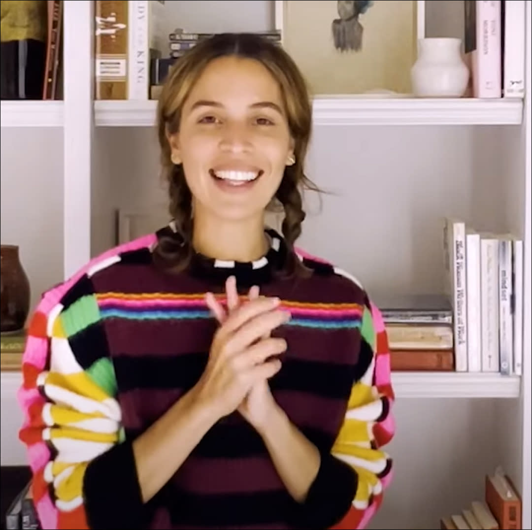  Cleo Wade smiling and standing in front of her bookshelves. 