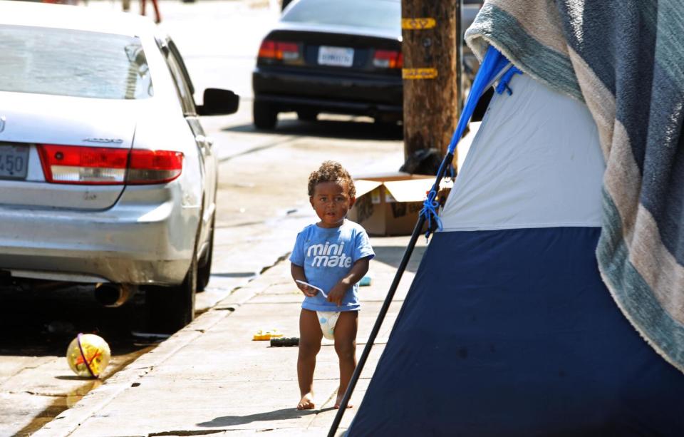 A migrant child in diapers stands barefoot in front of his family's tent