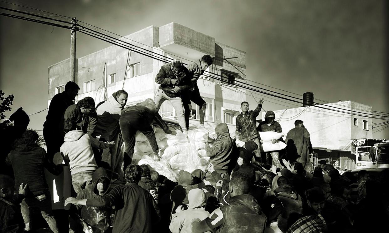 <span>A crowd of desperate people take food from trucks in an early morning convoy heading for Nasser hospital in Khan Younis.</span><span>Photograph: Christopher Black/WHO</span>