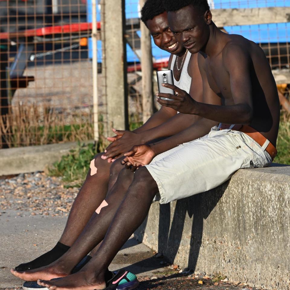 Two migrants sit on a wall drying their feet - Steve Finn