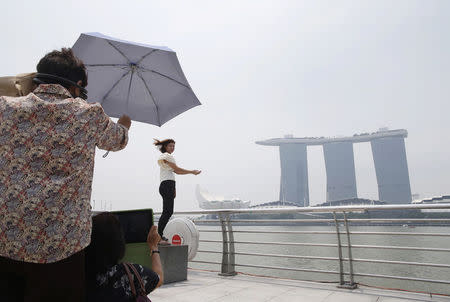 Tourists pose for photos with the Marina Bay Sands casino and resort (background) during haze in Singapore September 15, 2014. REUTERS/Edgar Su