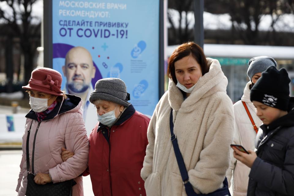 A group of people some of them wearing face masks walk past the poster showing a portrait of Dr. Denis Protsenko and words reading "Get vaccinated against covid-19!!" Near a vaccination point at VDNKh, The Exhibition of Achievements of National Economy in Moscow, Russia, Friday, April 2, 2021. Moscow is one of the few places in the world where one can get vaccinated against COVID-19 within hours of deciding to do so. To boost the demand, officials in Moscow this week started offering 1,000-ruble ($13) coupons to people over 60 for getting vaccinated. (AP Photo/Alexander Zemlianichenko)