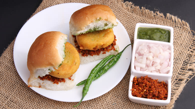 Two vada pav sandwiches with condiments