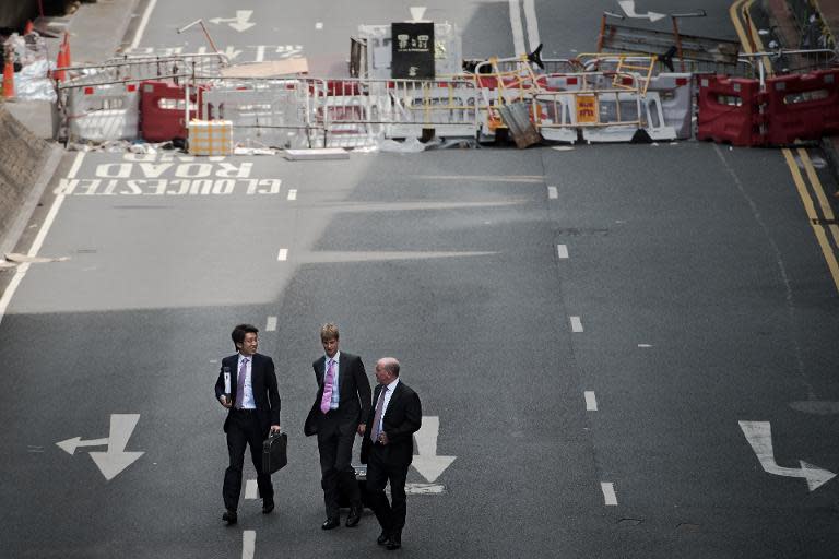 Businessmen walk on a barricaded road at the pro-democracy protesters camp site in the Admiralty district of Hong Kong on October 30, 2014