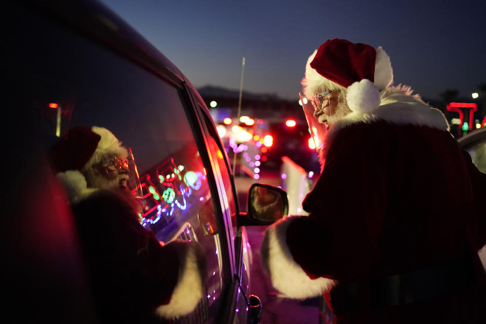 Charlie Bush, dressed as Santa Claus, wears a face shield as a precaution against coronavirus as he greets people waiting in their cars at Glittering Lights, a drive-thru holiday lights display, Thursday, Dec. 10, 2020, in Las Vegas. In this socially distant holiday season, Santa Claus is still coming to towns (and shopping malls) across America but with a few 2020 rules in effect. (AP Photo/John Locher)