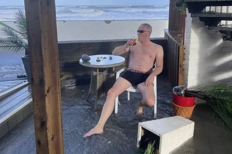 Pictured: Rob Braddick, 52, sat drinking a pint as his pub is flooded by high tides and battered by strong winds