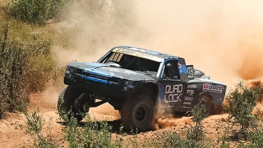 a black truck racing on a dusty dirt road