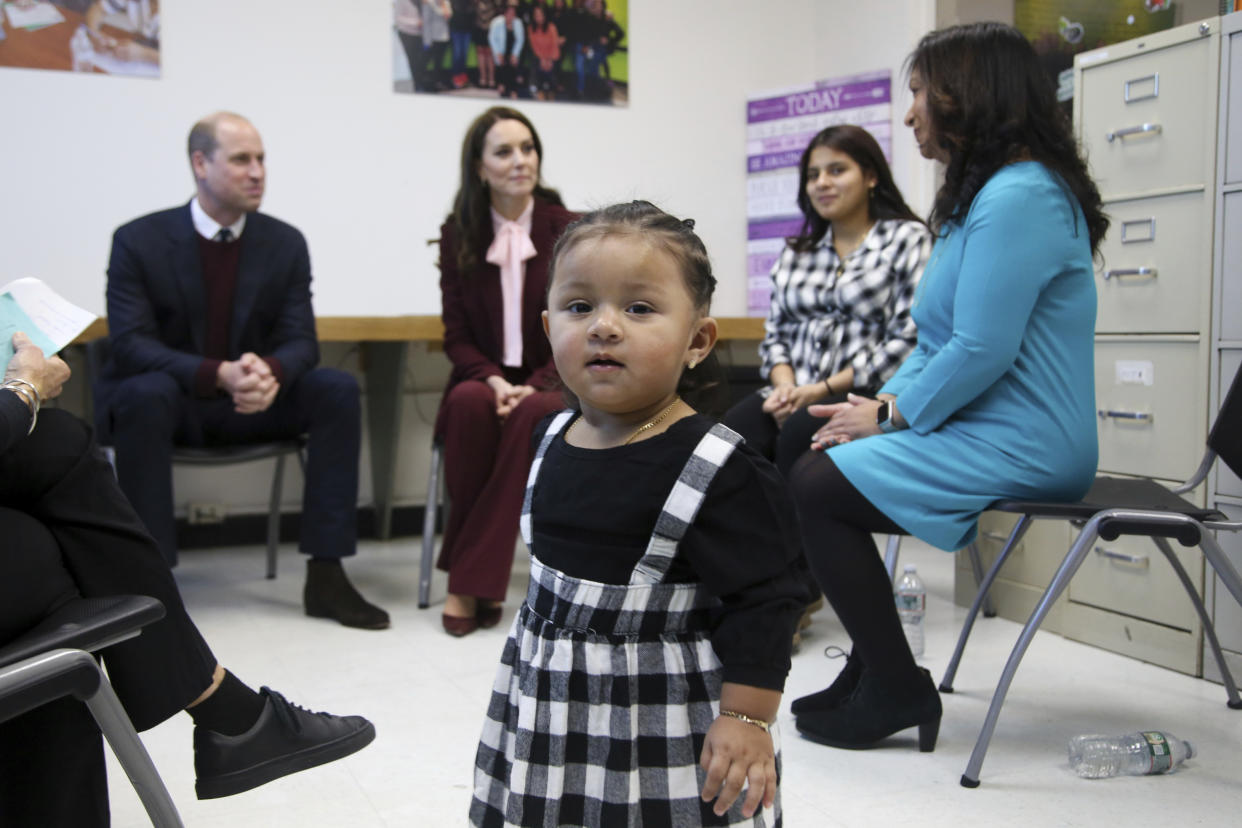 Sofia, 16 months, approaches media as Britain's Prince William and Kate, Princess of Wales, speak with her mother Katherine and Young Mother's Program director Sunindiya Bhalla, right, during a tour of Roca Thursday, Dec. 1, 2022, in Chelsea, Mass. (AP Photo/Reba Saldanha, Pool)