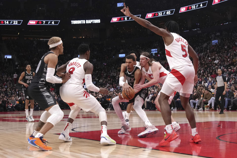 San Antonio Spurs center Victor Wembanyama (1) looks to pass the ball despite pressure from Toronto Raptors forward Kelly Olynyk, second from right, during first-half NBA basketball game action in Toronto, Monday Feb. 12, 2024. (Chris Young/The Canadian Press via AP)