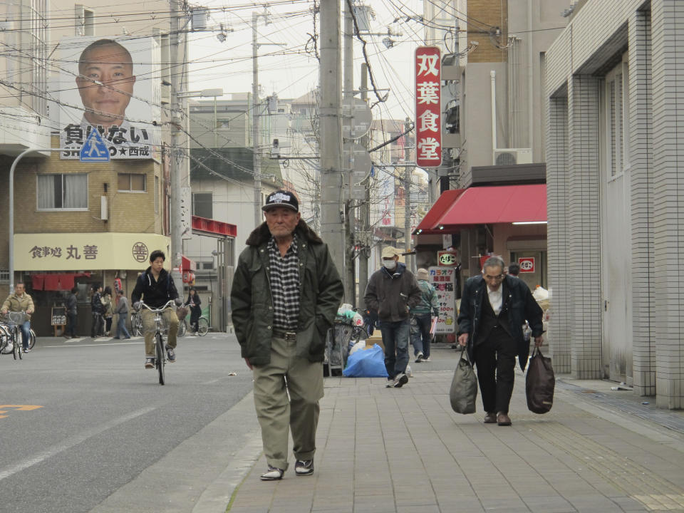 In this Sunday, March 16, 2014 photo, men walk in Kamagasaki, Osaka, western Japan. Japan’s biggest slum, Kamagasaki, is visible just blocks from bustling restaurants and shops in Osaka, the country’s second-largest city. But it cannot be found on official maps. Nor did it appear in the recent Osaka Asian Film Festival, after the director of a new movie that is set in the area pulled it, accusing city organizers of censorship. Osaka officials asked Shingo Ota to remove scenes and lingo that identify the slum, on the grounds that it was insensitive to residents. (AP Photo/Mari Yamaguchi)