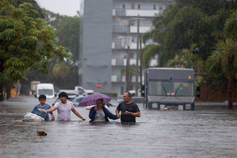  Personas caminan por una calle inundada mientras evacuan el 12 de junio de 2024, en Hollywood, Florida.