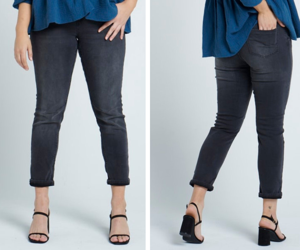 A woman wears black washed ankle length jeans with a black strappy heel against a pale blue background.