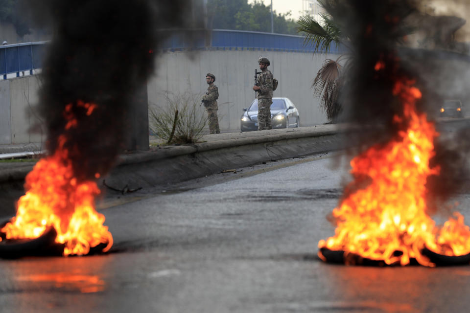 Lebanese army soldiers stand in front of burning tires blocking a main highway that leads to Beirut's international airport during a protest against the increasing prices of consumer goods and the crash of the local currency in Beirut, Lebanon, Monday, Nov. 29, 2021. (AP Photo/Hussein Malla)