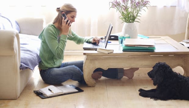 Mid adult woman sitting on floor, leaning on sofa, talking on, using laptop, side view