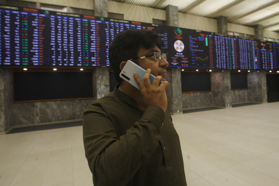 A broker talks on his cell phone while monitoring a stock index on a big screen at the Pakistan Stock Exchange, which responded positively after the news of an International Monetary Fund bailout package, in Karachi, Pakistan, Thursday, July 14, 2022. The IMF said Thursday it had reached a preliminary agreement with Pakistan to revive a $6 billion bailout package for this impoverished Islamic nation, which has been facing a serious economic crisis since last year. (AP Photo/Fareed Khan)