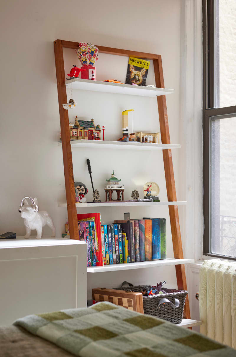 Books and toys on wood and white ladder bookcase in white room.