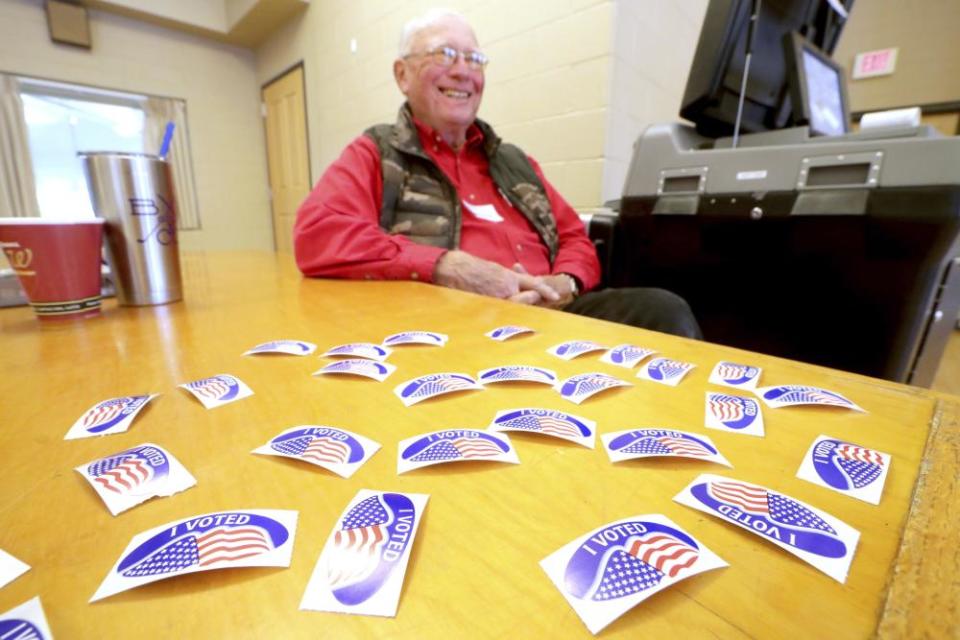 FILE - In this Feb. 18, 2020 file photo poll worker Bill Martens mans the ballot machine and “I Voted: stickers at the Hart Park Muellner Building in Wauwatosa, Wis. Pressure on Gov. Tony Evers to postpone Wisconsin’s spring election is mounting due to the threat of the coronavirus. Civil rights and voting rights groups are planning a conference call with reporters on Monday, March 23, 2020, to demand that Evers issue an emergency order delaying the April 7 election. (Mike De Sisti/Milwaukee Journal-Sentinel via AP, File)