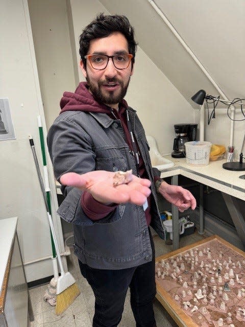 Pratt Munson artist-in-residence Felipe Lopez holds up a miniature pedestal made of homemade hemp paper, demonstrating how the pedestal comes to sag and lean over time.