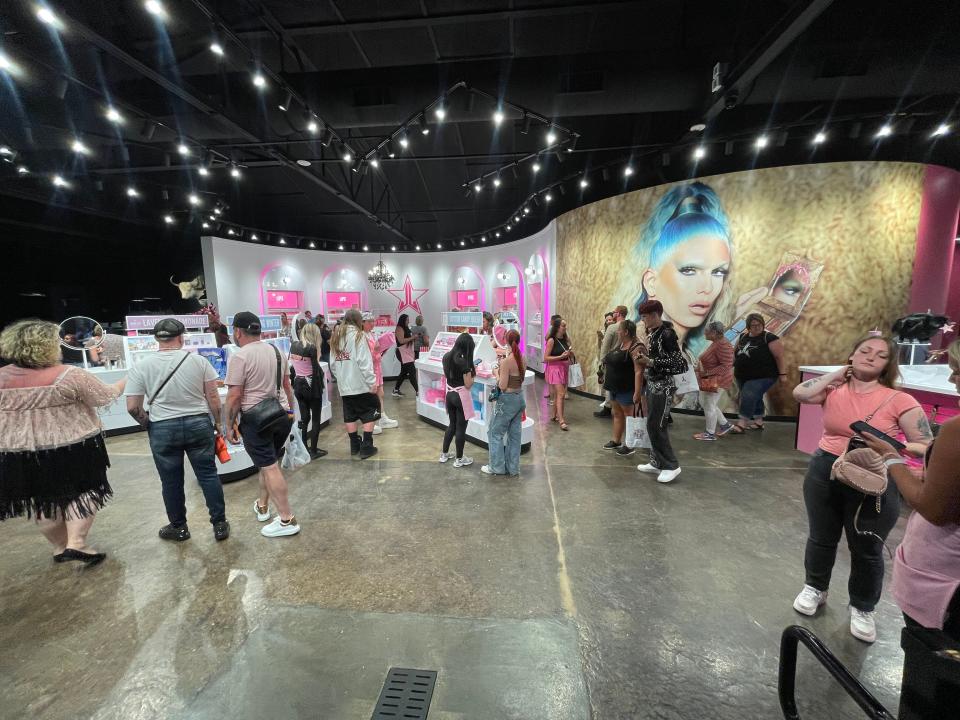 Concrete floors, black ceilings and light bulbs inside the Jeffree Star store, filled with individuals walking around and shopping in front of a large poster of Jeffree Star