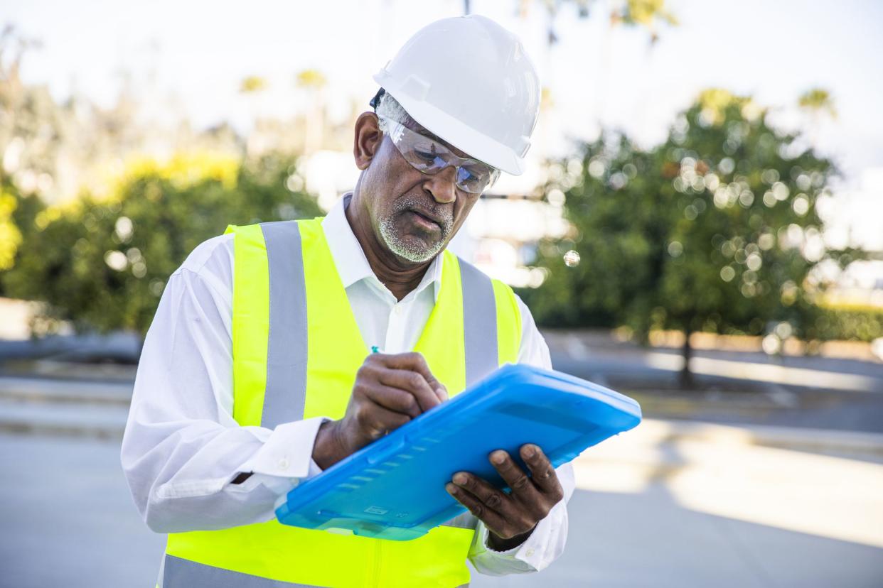 A senior black male construction site manager visually inspects a building project