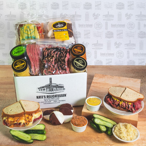 dinner box on top of wooden countertop with sandwiches, sliced pickles, meat, and sauce