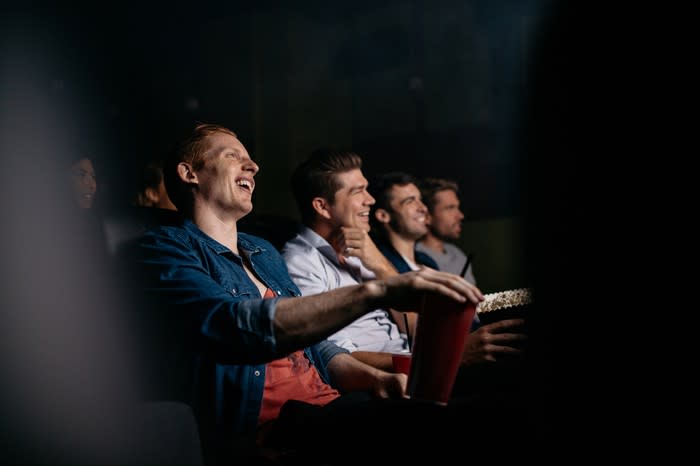 A row of men in a movie theater, with one reaching for his popcorn