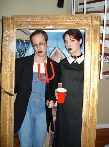 Two people inside a large frame recreating the "American Gothic" painting with goth clothes and makeup