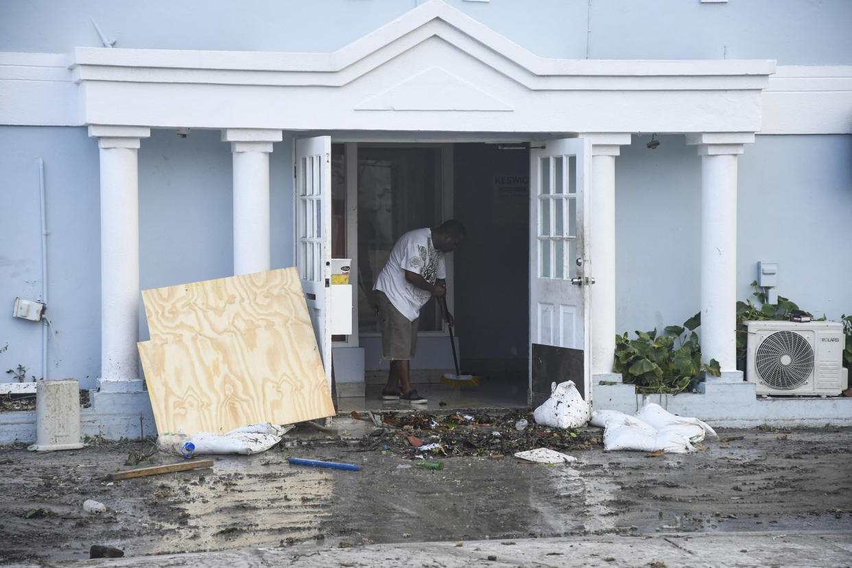 A man uses a broom to clear water from the front of a damaged restaurant in Christ Church. 