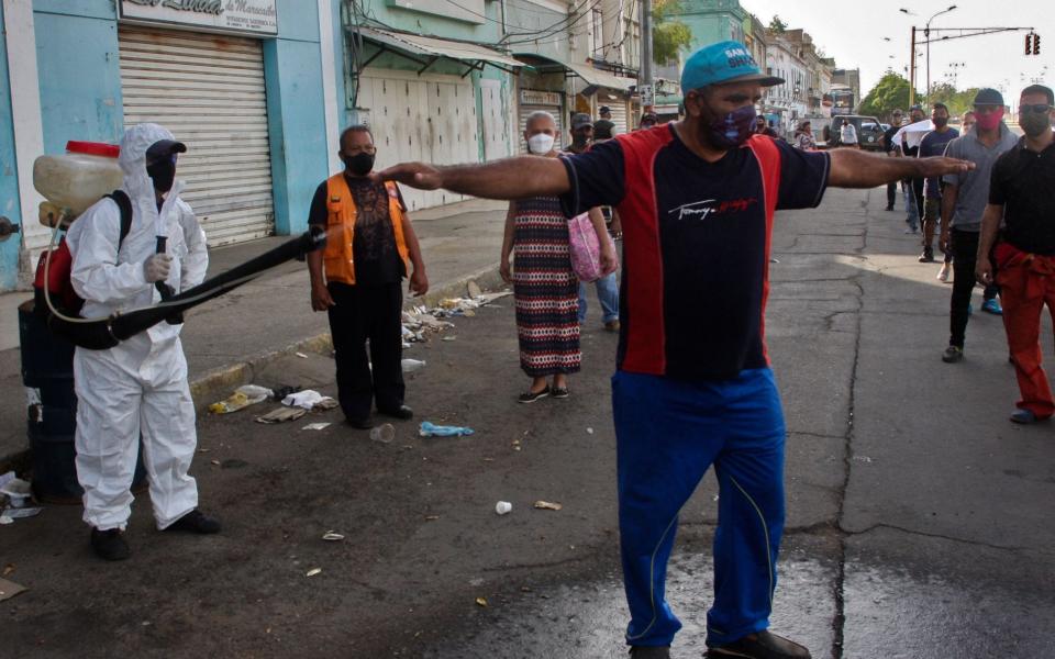 A municipal worker disinfects a salesman who works outside the flea market in Maracaibo, Zulia State, Venezuela - AFP