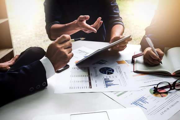 Three people sitting at a table reviewing financial charts.