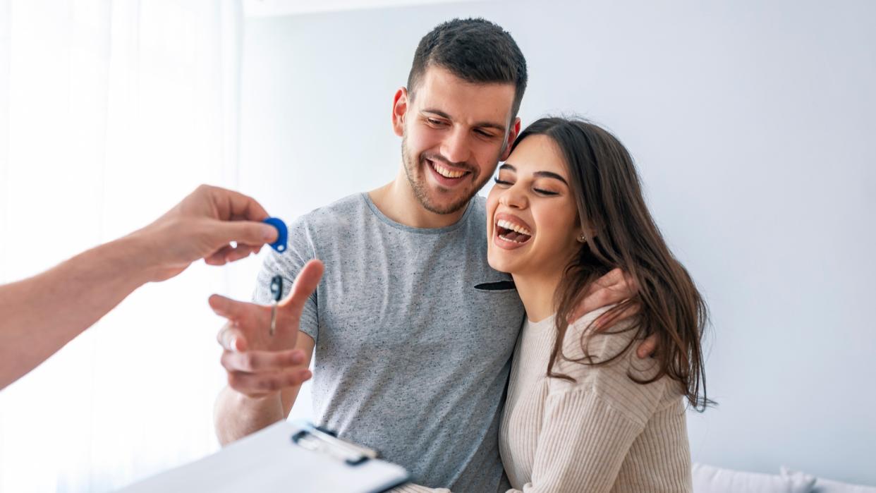 Happy couple is taking keys from their new house from hand of estate agent. 