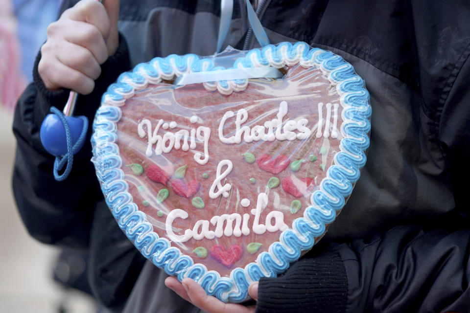 A Royal fan carries a gingerbread heart with the inscription "King Charles III & Camila" and waits in the rain at the Rathausmarkt in front of Hamburg City Hall for the arrival of the British royals, Friday, March 31, 2023 . At the end of their three-day trip to Germany, Britain's King Charles III and Camilla Queen Consort visit the Hanseatic city of Hamburg. (Marcus Brandt/dpa via AP)