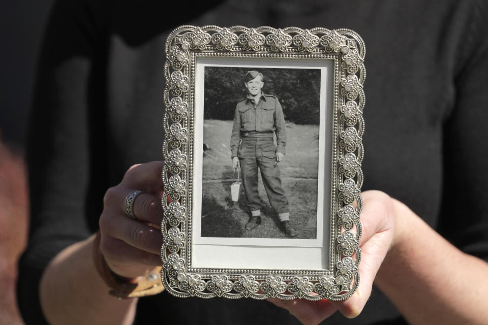 FILE - In this Wednesday, April 8, 2020, file photo, Kelly Adsero holds a family photo of her grandfather Bill Chambers that shows him when he was a young solider in the Canadian Army. Chambers, 97, died March 14, 2020, He wasn't obviously ill, but tested positive for the new coronavirus after he died. The passage of a milestone — 100,000 lives lost due to the coronavirus in the United States — has brought attention to how news organizations are trying to tell the stories behind the numbers. (AP Photo/Ted S. Warren, File)