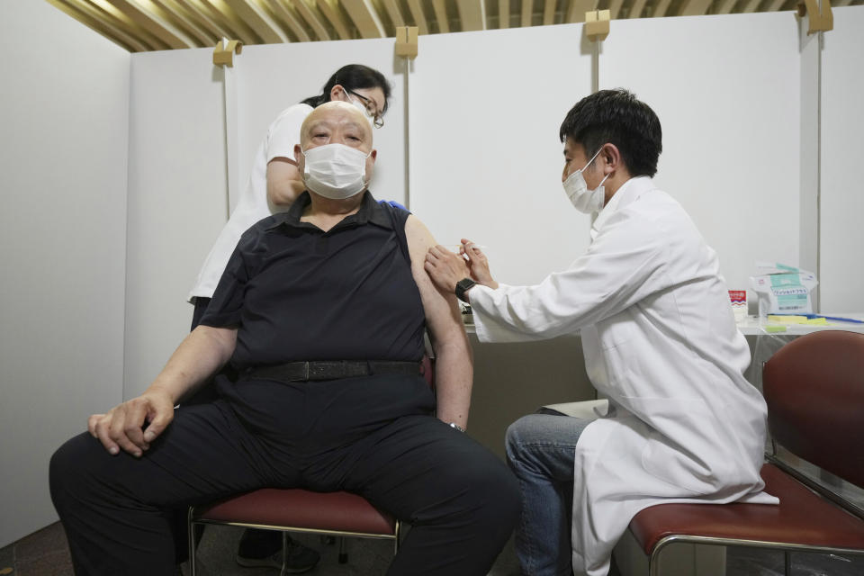 FILE - In this May 24, 2021, file photo, former sumo stable master Chiganoura, left, receives his first dose of Pfizer's COVID-19 vaccine at the Ryogoku Kokugikan sporting arena. The arena, mainly used for sumo wrestling tournaments, is being used as a temporary inoculation venue for residents over 65 years old in Tokyo. Japan, seriously behind in coronavirus vaccination efforts, is scrambling to boost daily shots as the start of the Olympics in July closes in. (AP Photo/Eugene Hoshiko, File)