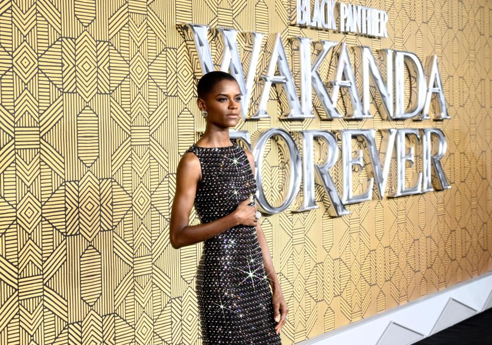 Letitia Wright in black crystal dress in front of gold Wakanda Forever sign