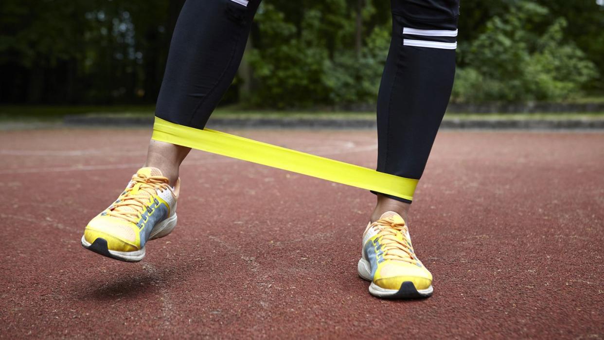 legs of young woman training in park, stretching resistance band