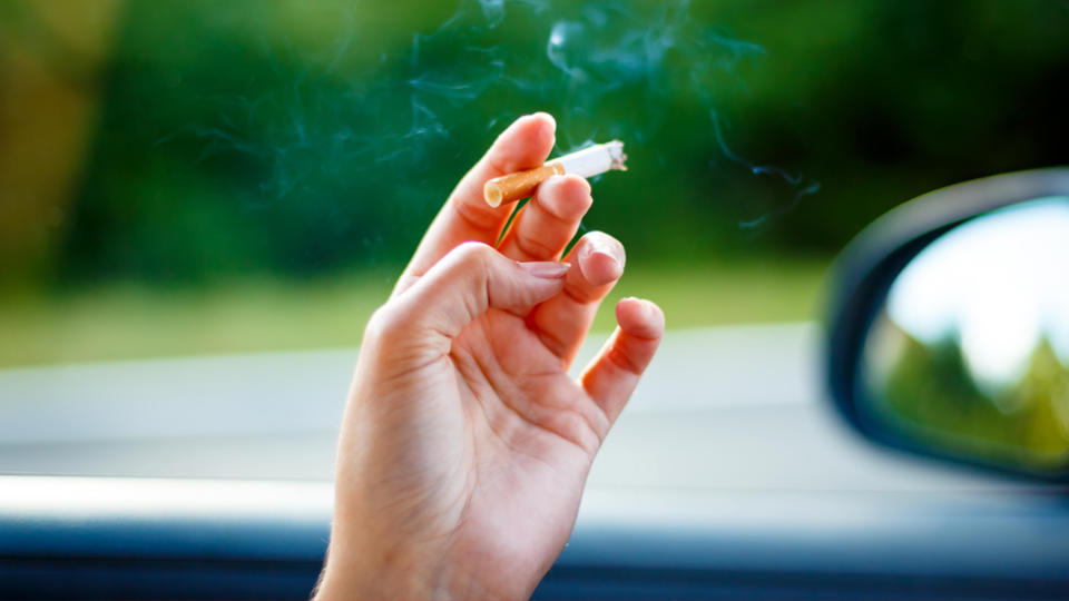 A person in a car with a lit cigarette. During a total fire ban, tossing a lit cigarette out the window will end with a hefty fine.