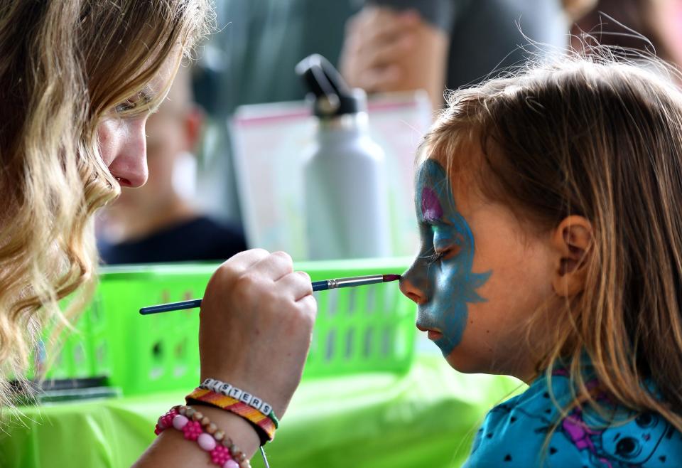 Maggie Mussler, 17, of Apple Tree Arts paints a blue bunny on the face of Zoe Herbert, 6, of Grafton during the Grafton Farmers Market at the Grafton Municipal Town Building on 30 Providence Road.